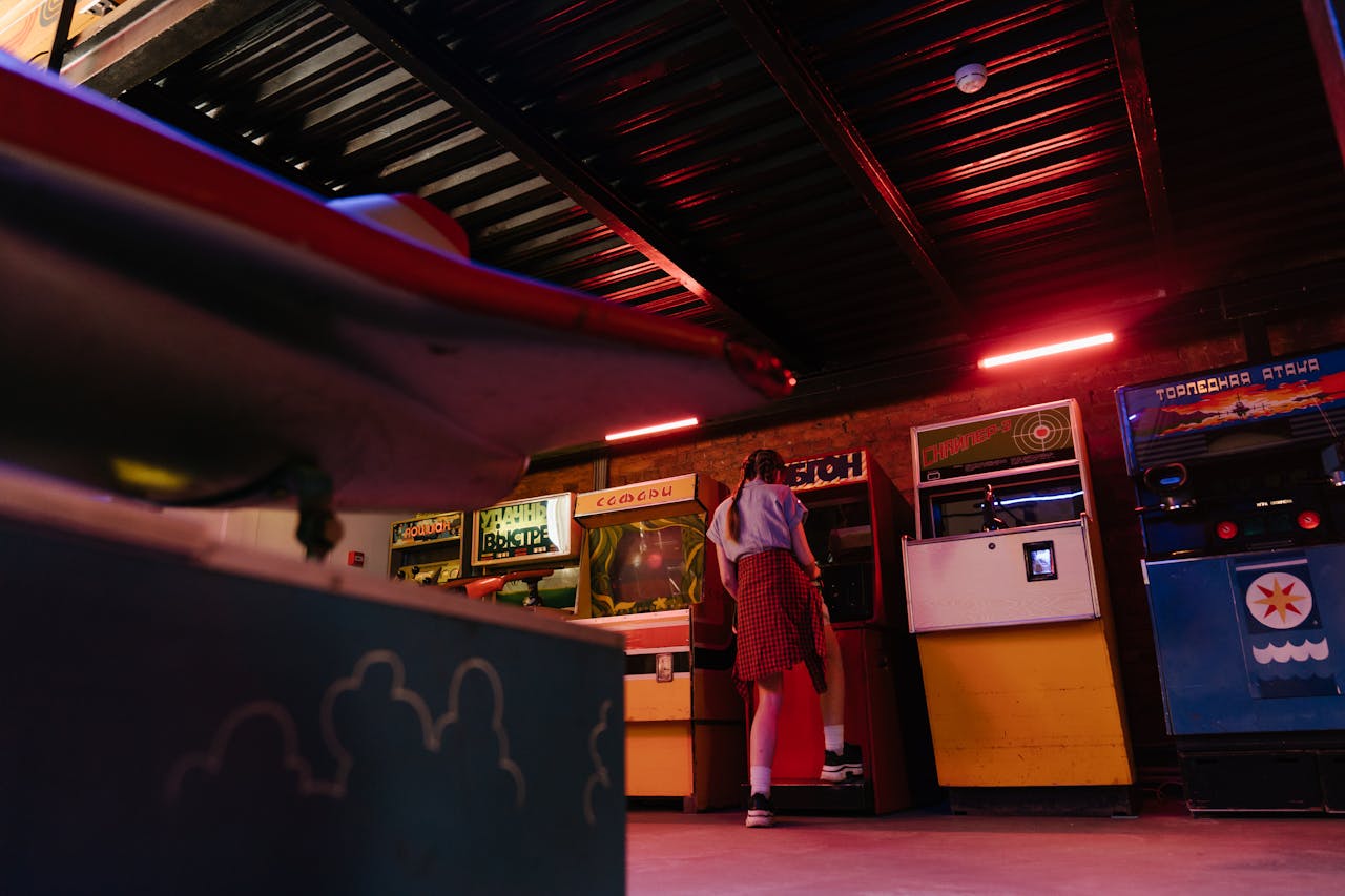 our-story-01 Teen girl enjoying retro arcade games in a dimly lit indoor amusement area.